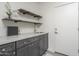 Stylish laundry room with gray cabinetry, marble countertop, sink, floating wood shelves and white door at 28437 N 112Th Way, Scottsdale, AZ 85262