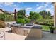 Outdoor kitchen with built-in grill, counter space, and seating area surrounded by lush landscaping at 12976 W Plum Rd, Peoria, AZ 85383