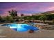 Backyard oasis illuminated with underwater lights and dusk sky, featuring a freeform pool with waterfall and spa at 12976 W Plum Rd, Peoria, AZ 85383