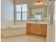 A bathtub with a window sits next to a wooden vanity with a large mirror at 20472 W Daniel Pl, Buckeye, AZ 85396