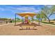 Community playground featuring a covered play structure, swings, and seesaw on a sandy base at 21616 E Calle De Flores --, Queen Creek, AZ 85142