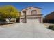Tan two-story home featuring a spacious three-car garage and a mature tree in the front yard at 23104 W Kimberly Dr, Buckeye, AZ 85326