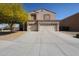 Tan two-story home featuring a spacious three-car garage and a mature tree in the front yard at 23104 W Kimberly Dr, Buckeye, AZ 85326