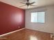 Simple bedroom with hardwood floors, ceiling fan, red accent wall, and a window for natural light at 11403 W Rosewood Dr, Avondale, AZ 85392