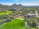 Aerial view of the house, golf course, and clubhouse nestled into the desert landscape with mountain views at 28990 N White Feather Ln # 185, Scottsdale, AZ 85262
