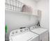 Well-lit laundry room features front loading washer and dryer with shelving, providing organized laundry solutions at 39959 W Williams Way, Maricopa, AZ 85138