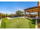 This backyard features a pool, a putting green, an outdoor kitchen, and a covered patio at 9059 E Leonora St. St, Mesa, AZ 85207