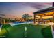This backyard features a pool, a putting green, an outdoor kitchen, and a covered patio at dusk at 9059 E Leonora St. St, Mesa, AZ 85207