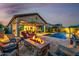 This backyard features a pool, seating around a fire pit, and an outdoor dining area at twilight at 9059 E Leonora St. St, Mesa, AZ 85207