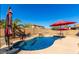 Clear blue pool with rock features, shaded by red umbrellas, offers a tranquil backyard retreat at 13628 W San Miguel Ave, Litchfield Park, AZ 85340
