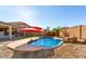 Sparkling pool with a rock waterfall and two red umbrellas is surrounded by desert landscaping and ample patio space at 13628 W San Miguel Ave, Litchfield Park, AZ 85340