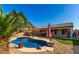 Relaxing pool with a rock feature and palm tree, enhanced by artificial turf and red umbrellas for shade at 13628 W San Miguel Ave, Litchfield Park, AZ 85340