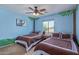 Vibrant blue bedroom featuring two comfortable beds, tree-themed wall art, and a ceiling fan at 15324 W Windsor Ave, Goodyear, AZ 85395