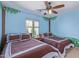 Bright blue bedroom with two beds, charming tree-themed wall art, and a sunlit window at 15324 W Windsor Ave, Goodyear, AZ 85395