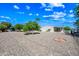Expansive gravel backyard with mature trees, a fire pit, and a manufactured home under a bright, partly cloudy sky at 3160 E Main St # 110, Mesa, AZ 85213