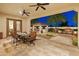 Covered patio with dining table, chairs, ceiling fans, outdoor kitchen, and a cozy outdoor fireplace at 7425 W Caro Rd, Glendale, AZ 85308