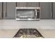 Close-up of modern stainless steel microwave and gas cooktop over gray cabinets and white quartz countertops at 13305 W Colter St, Litchfield Park, AZ 85340