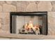 Close up of a fireplace with faux logs burning, inside a light stone fireplace, creating a warm ambiance at 22318 N Pico Ct, Sun City West, AZ 85375