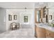 Bright bathroom featuring a soaking tub, stone floors, framed mirrors, and a sitting chair at 7525 N Shadow Mountain Rd, Paradise Valley, AZ 85253