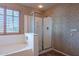 Bathroom showcasing a soaking tub, glass shower, and shuttered window with floral patterned wallpaper at 10517 W La Reata Ave, Avondale, AZ 85392