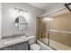 This bathroom features a granite countertop vanity, round mirror and a glass-door shower-tub at 11666 N 28Th Dr # 295, Phoenix, AZ 85029