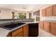 A kitchen sink area featuring oak cabinets, a black dishwasher, and a view of a well-maintained backyard at 13213 W Jacobson Dr, Litchfield Park, AZ 85340