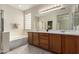Bathroom featuring dual sinks, wooden cabinets, a glass block window, a soaking tub, and a stand up shower at 29399 N 67Th Ave, Peoria, AZ 85383