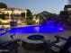 Beautifully lit pool with a rock waterfall, fire pit, and shaded pergola, creating a magical outdoor space at night at 3067 E Trigger Way, Gilbert, AZ 85297