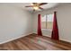 Bright bedroom with wood-look floors, a ceiling fan, and a window dressed with dark-red curtains at 4746 W Taro Dr, Glendale, AZ 85308