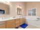 Bright bathroom featuring a double sink vanity, a large mirror, a bathtub, and natural light from the window at 3060 E Hope St, Mesa, AZ 85213