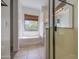 Bathroom with a soaking tub, window with blinds, and glass enclosed shower, all enhanced by neutral tile flooring at 6941 E Snowdon St, Mesa, AZ 85207