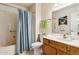 Bathroom features vanity, sink and mirror adjacent to a toilet and shower with blue curtain at 12726 W Copperstone Dr, Sun City West, AZ 85375