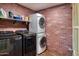 Laundry room with stacked washer/dryer, red brick accent wall, and shelving at 2424 E Ivy St, Mesa, AZ 85213