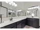 Bathroom with dark cabinets, double sinks, large mirror, and a glass-enclosed shower featuring decorative tiling at 16235 W Cottonwood St, Surprise, AZ 85374