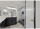 A bright bathroom with a dark wood vanity, dual sinks, and a glass-enclosed shower with decorative black tile at 16235 W Cottonwood St, Surprise, AZ 85374