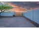 An enclosed backyard with a block fence, wooden gate, desert landscaping, and concrete driveway at sunset at 1644 W Roma Ave, Phoenix, AZ 85015