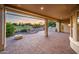 Covered brick patio overlooking a green view of the golf course at sunset with lush garden and mature trees at 22208 N San Ramon Dr, Sun City West, AZ 85375