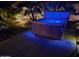 Backyard hot tub with glowing blue LED lights at night, surrounded by landscaping and a concrete patio at 45028 W Cypress Ln, Maricopa, AZ 85139