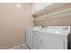 Functional laundry room boasts white appliances and shelving, enhancing organization and efficiency at 45028 W Cypress Ln, Maricopa, AZ 85139