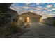 Front exterior featuring an arched entrance, a two-car garage, and desert landscaping under a beautiful sunset sky at 14916 W Georgia Dr, Surprise, AZ 85379