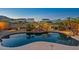 Inviting backyard pool featuring a rock waterfall, lush landscaping, and ambient lighting for evening enjoyment at 21104 W Sage Hill Rd, Buckeye, AZ 85396