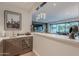 The wet bar has a small sink, countertop space, a built in wine cooler and pendant lights above it with access to the living area at 6142 E Alta Hacienda Dr, Scottsdale, AZ 85251