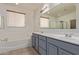 Bathroom featuring dual sinks, a soaking tub, and two large windows at 11952 W Overlin Ln, Avondale, AZ 85323