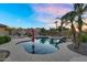 Backyard pool surrounded by landscaping, palm trees, and an outdoor firepit at sunset at 18822 E Flintlock Dr, Queen Creek, AZ 85142