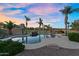 Stunning pool with rock waterfall feature, surrounded by lush landscaping and mature palm trees at sunset at 18822 E Flintlock Dr, Queen Creek, AZ 85142