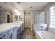 Bright bathroom featuring double sink vanity with framed mirrors, soaking tub with glass block window and tiled shower at 1950 W Park Pl, Chandler, AZ 85224