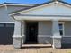 Inviting front entry with a covered porch featuring brick accents and a modern black front door at 17677 W Odeum Ln, Goodyear, AZ 85338