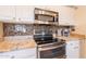 Close-up of the kitchen with stainless steel appliances, granite countertops, and mosaic tile backsplash at 43612 W Chambers Ct, Maricopa, AZ 85138