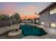 Backyard view of a gunite pool with waterfall feature surrounded by desert landscaping and swaying palm trees at dusk at 5004 W Kaler Dr, Glendale, AZ 85301
