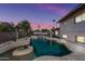 Backyard view of a gunite pool with waterfall feature surrounded by desert landscaping and swaying palm trees at dusk at 5004 W Kaler Dr, Glendale, AZ 85301
